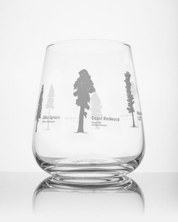 A Forest Giants Wine Glass by Cognitive Surplus with trees in it on a white surface.